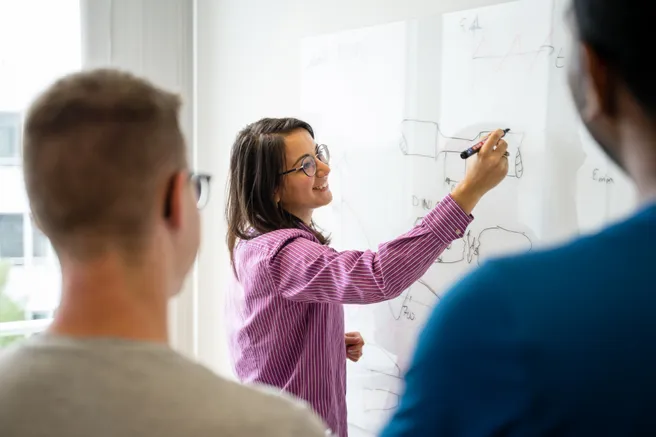 A woman draws a technical drawing on a whiteboard